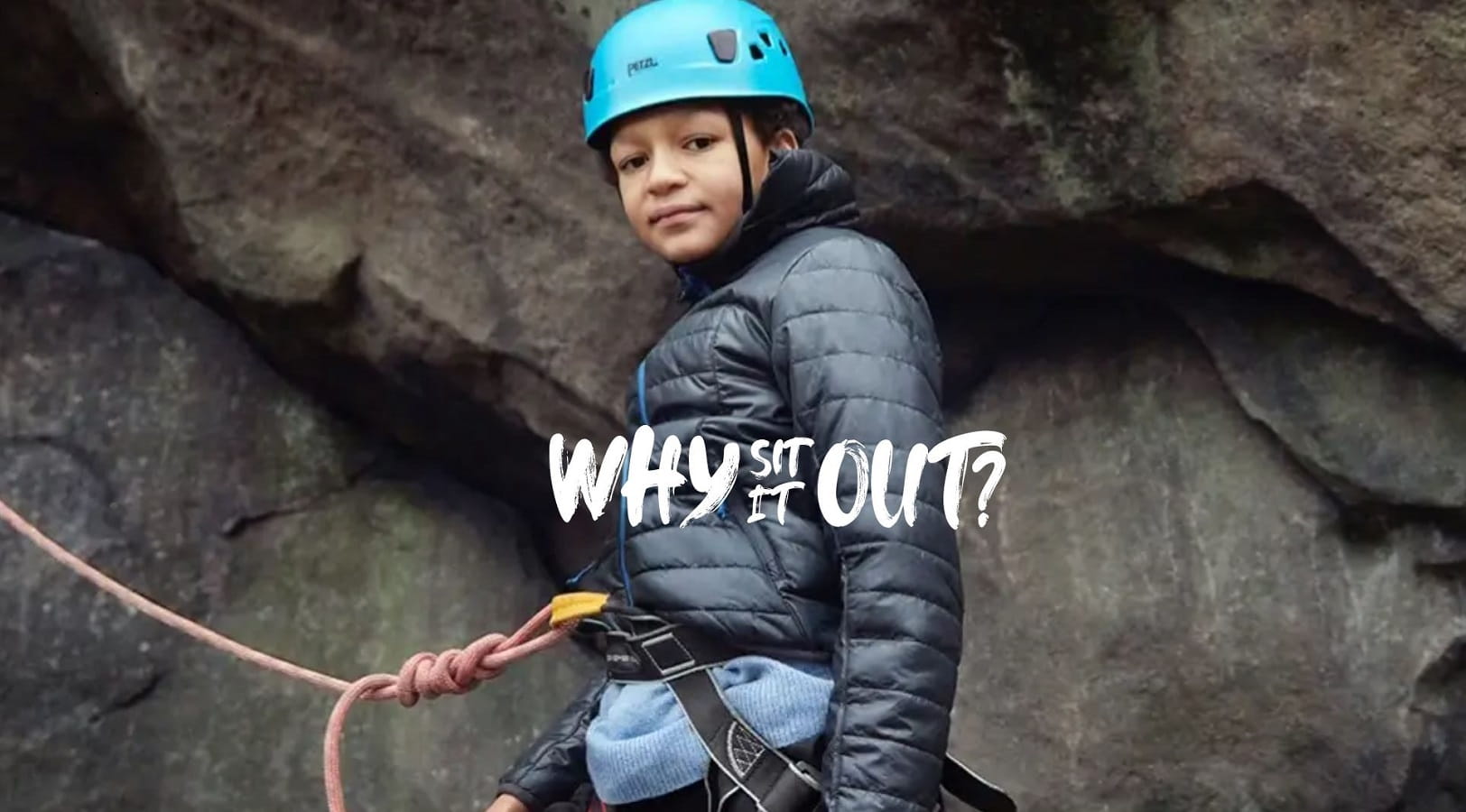 A boy with blue safety helmet and safety rope climbs a rock face