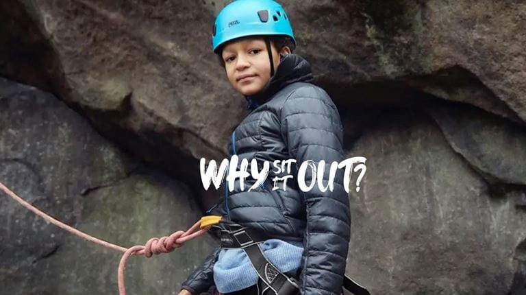 A boy with blue safety helmet and safety rope climbs a rock face