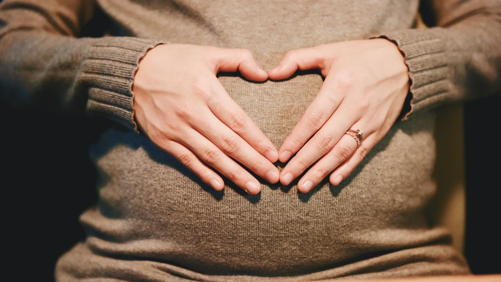 Pregnant mother earing brown jumper holds her tummy
