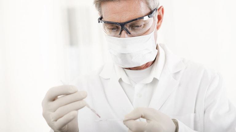 Male researcher taking a sample wearing goggles, face mask and gloves